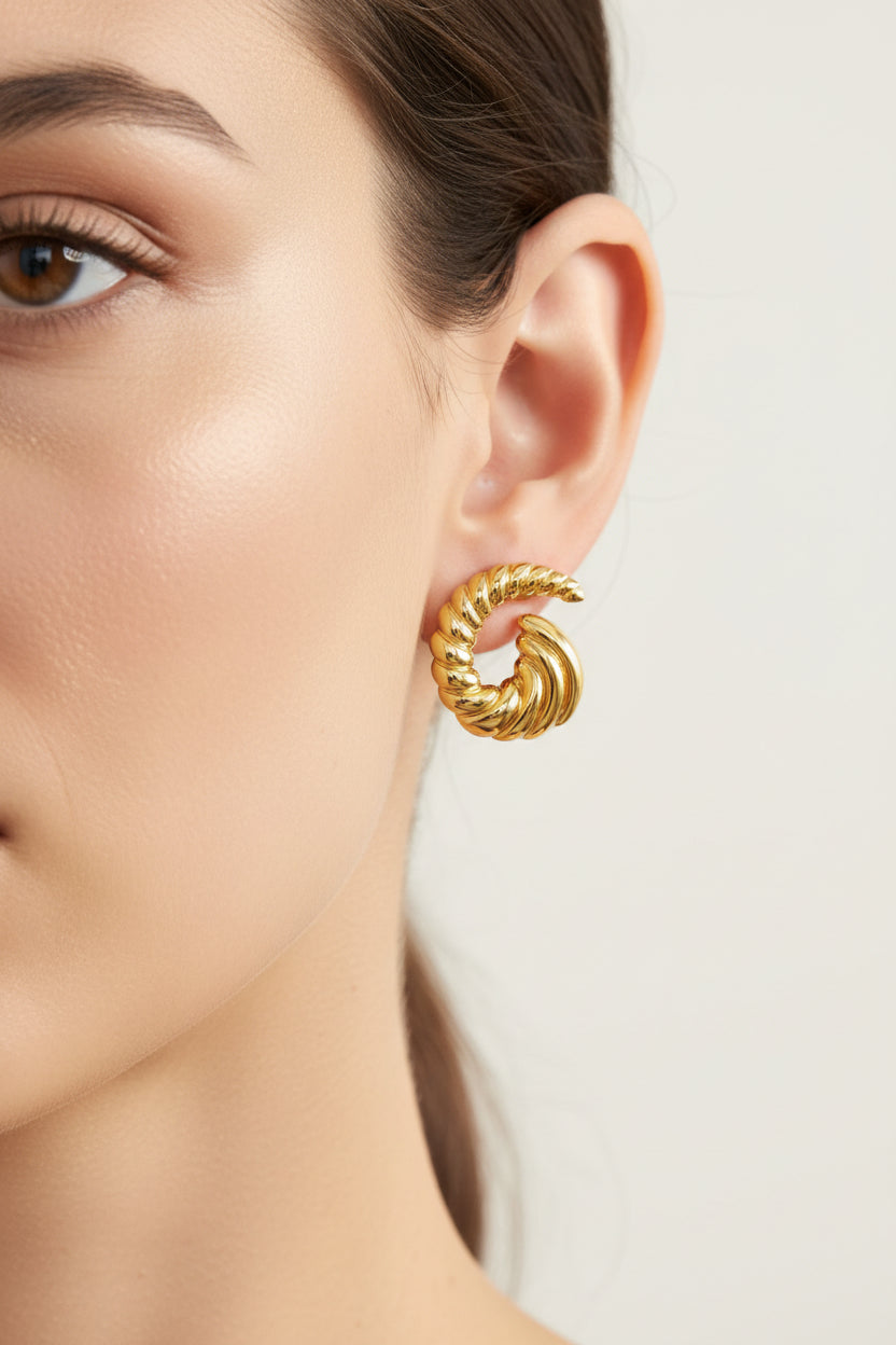 Open spiral swirl stud earrings worn on ear, showcasing modern sculptural swirl design with 18K PVD gold plated finish