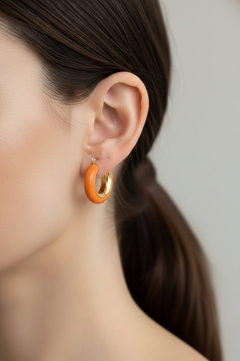 Close-up of orange enamel hoop earrings in 18K PVD gold plated stainless steel, showcasing a smooth glossy surface and modern colourful design.