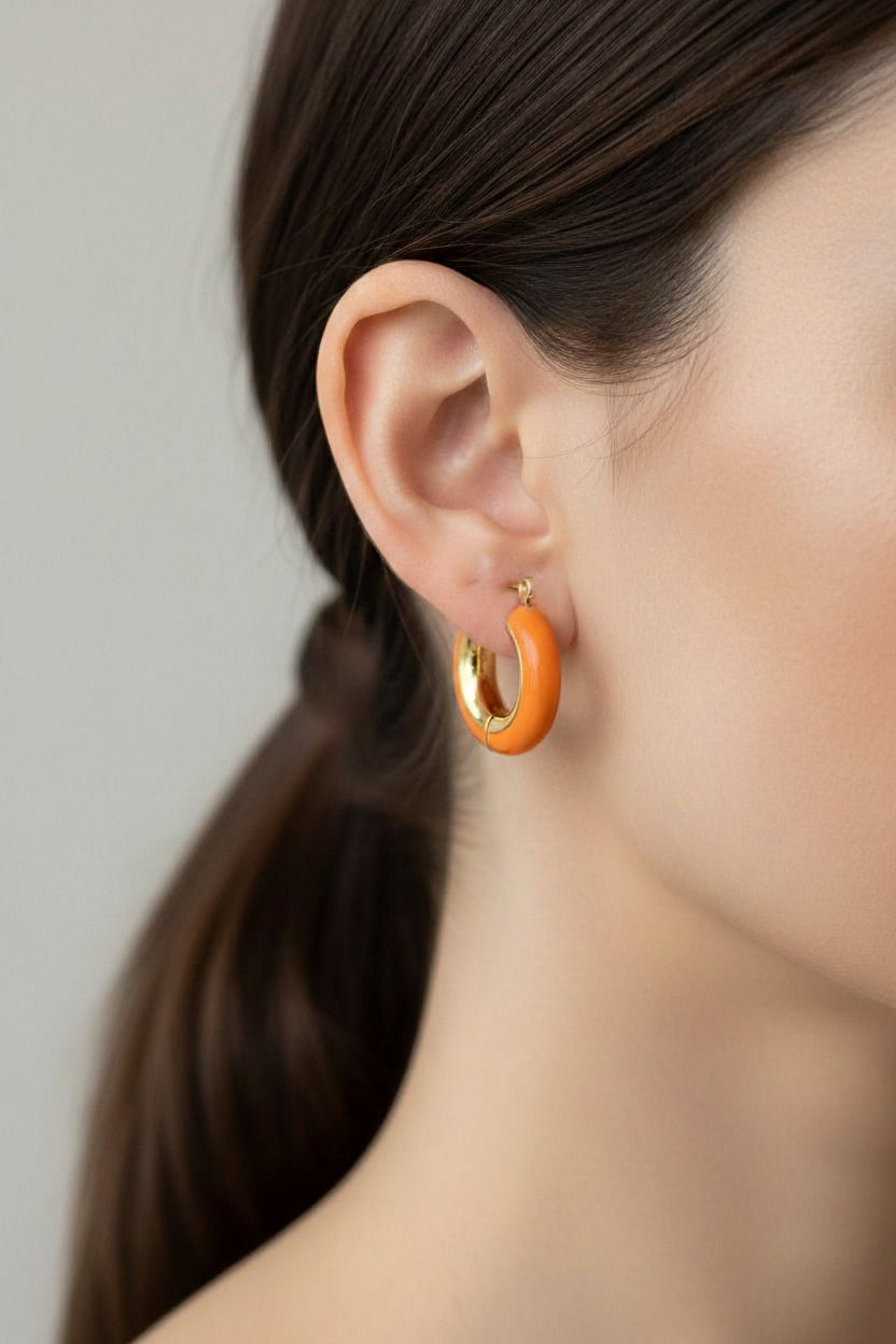 Orange enamel hoop earrings crafted from stainless steel with 18K PVD gold plating, featuring a glossy rounded silhouette and vibrant orange finish