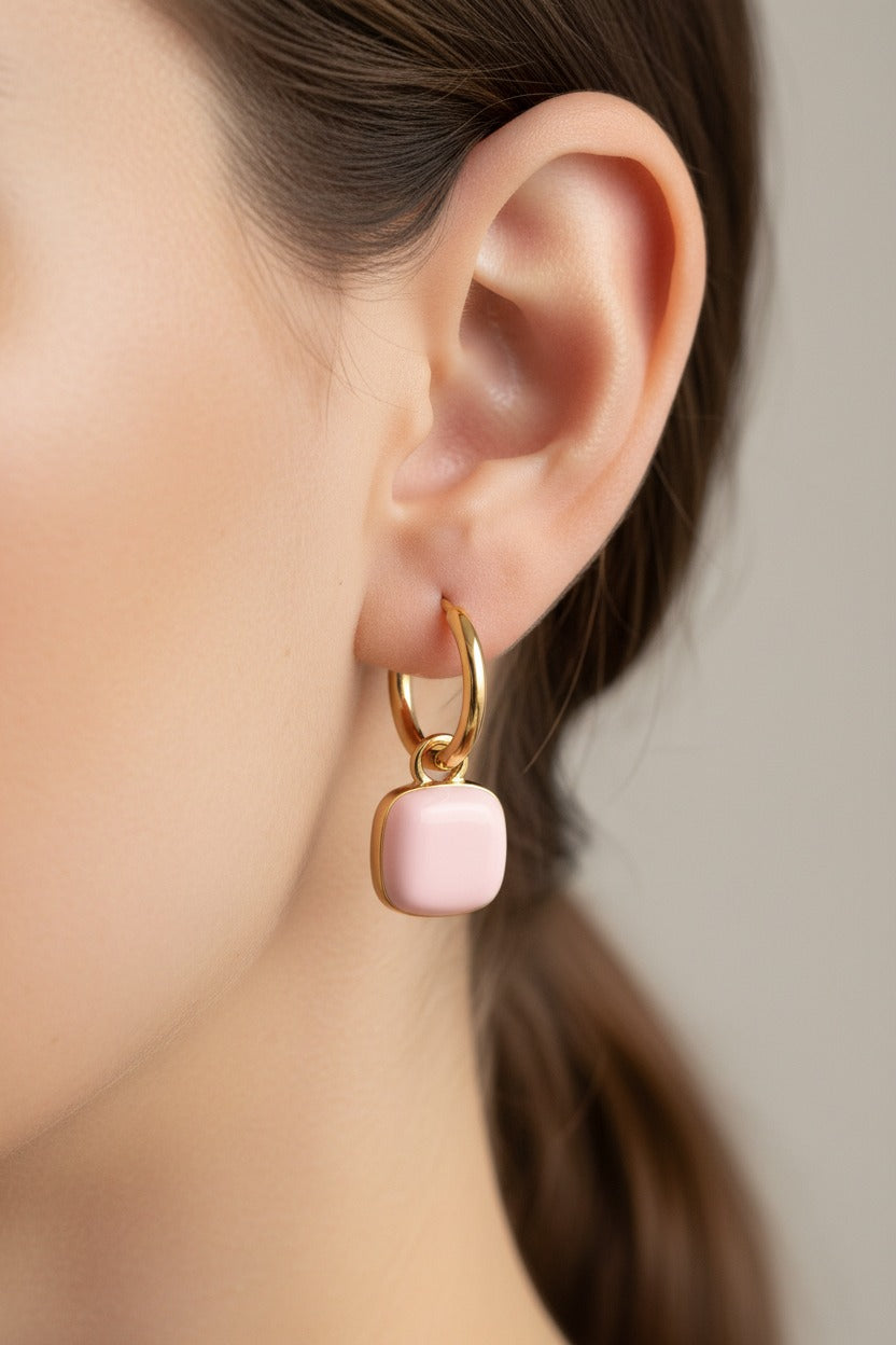 Pink charm drop hoop earrings in 18K PVD gold plated stainless steel worn on model ear.
