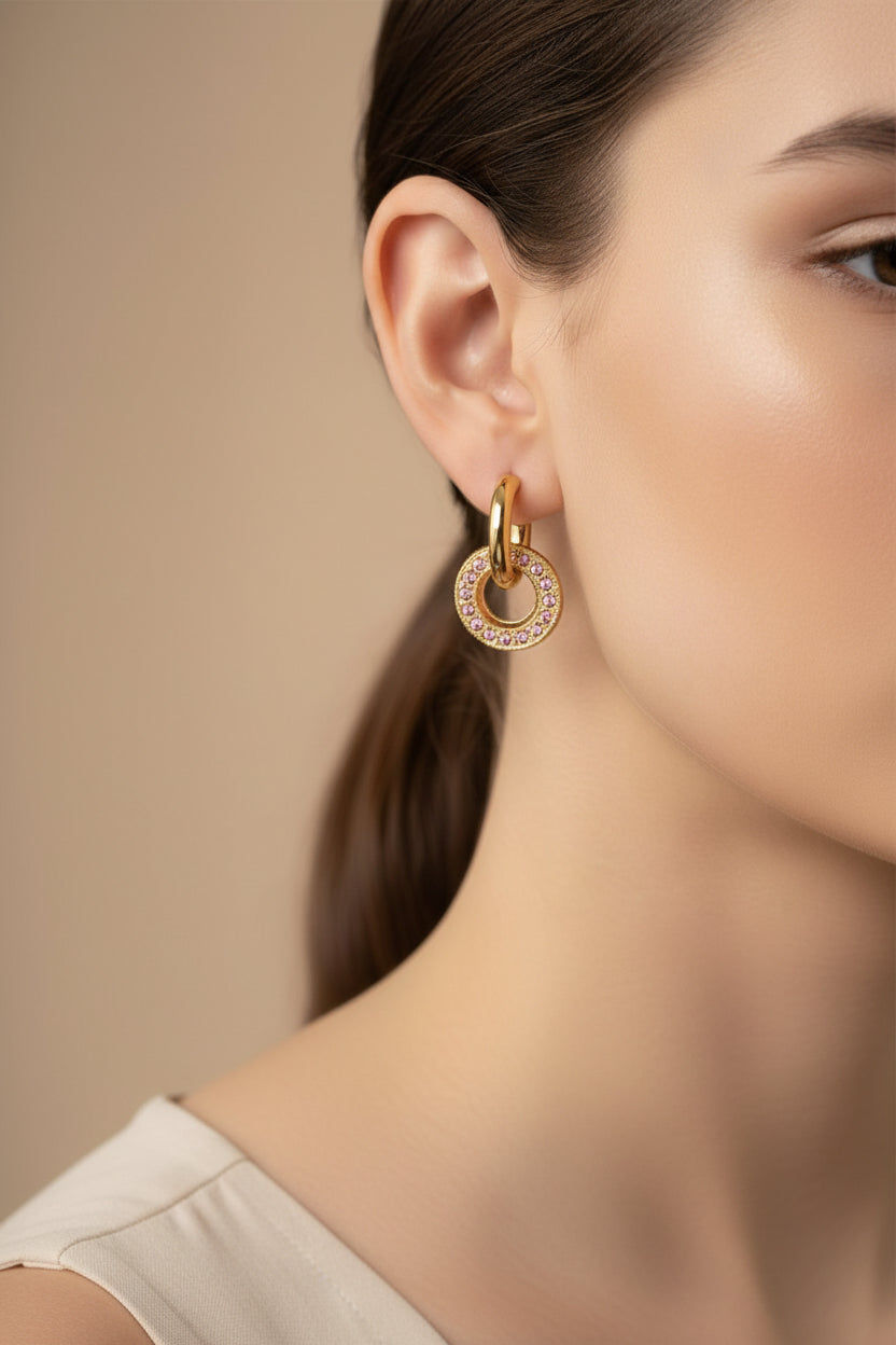 Close-up of hoop earrings with circle drop and pink crystal detailing in 18K PVD gold plated stainless steel, showcasing a polished finish and vibrant colour
