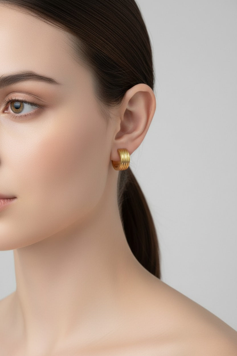 Ribbed huggie hoop earrings in 18K PVD gold plated stainless steel worn on model ear by GLISTIA