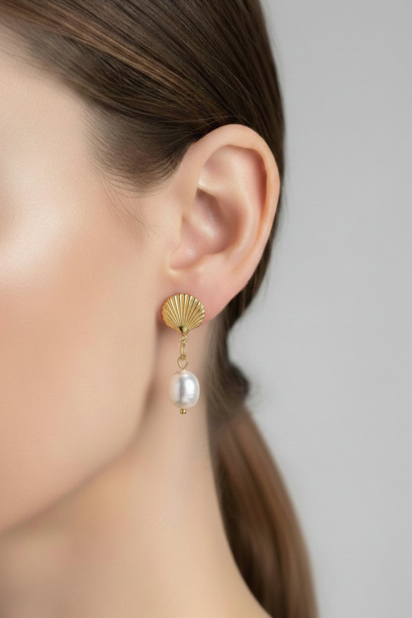 Close-up of gold shell drop earrings showcasing polished 18K PVD gold plating and a luminous pearl accent.