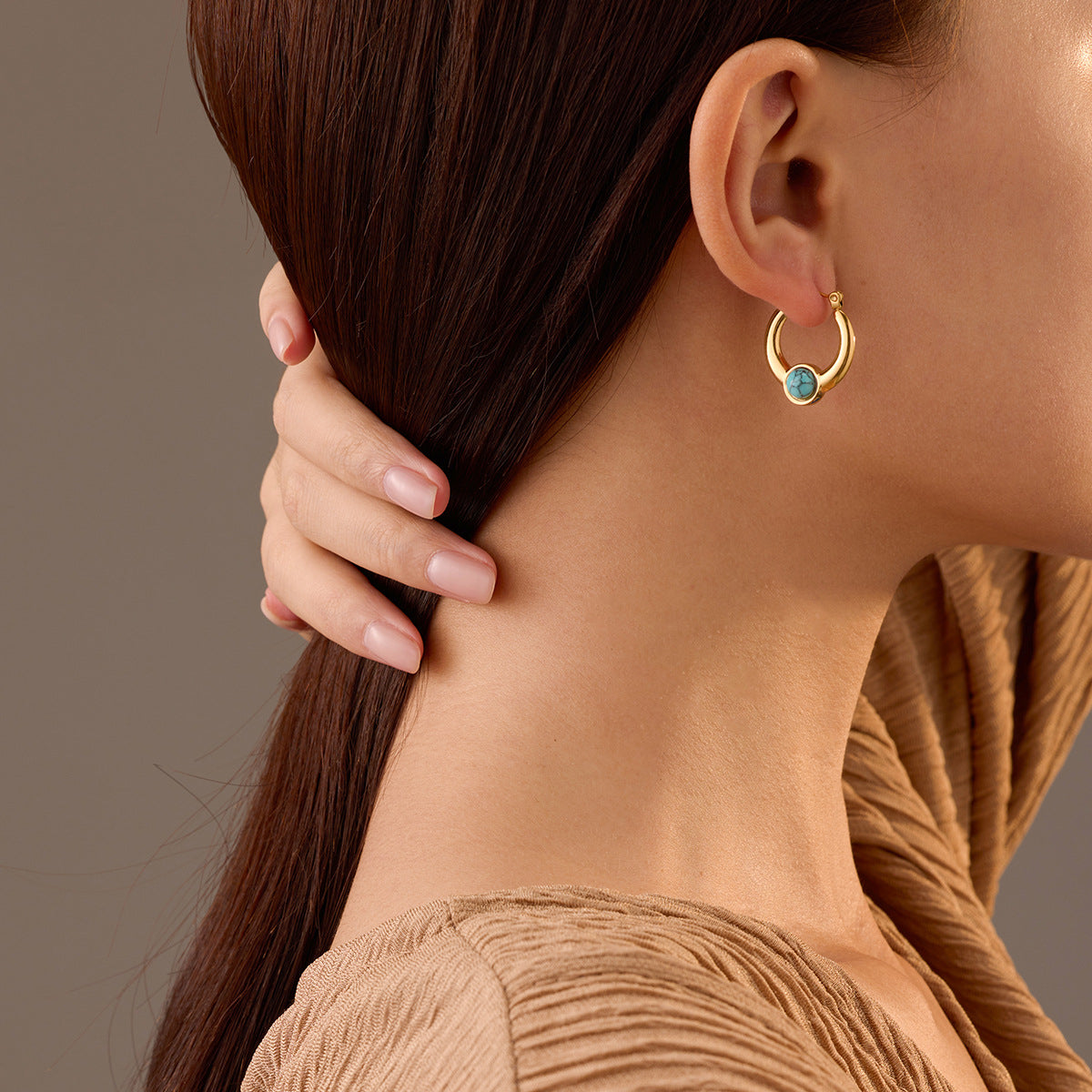 Close-up of a woman wearing small gold hoop earrings featuring turquoise stone accents, crafted from stainless steel with a polished PVD 18K gold-plated finish - GLISTIA.