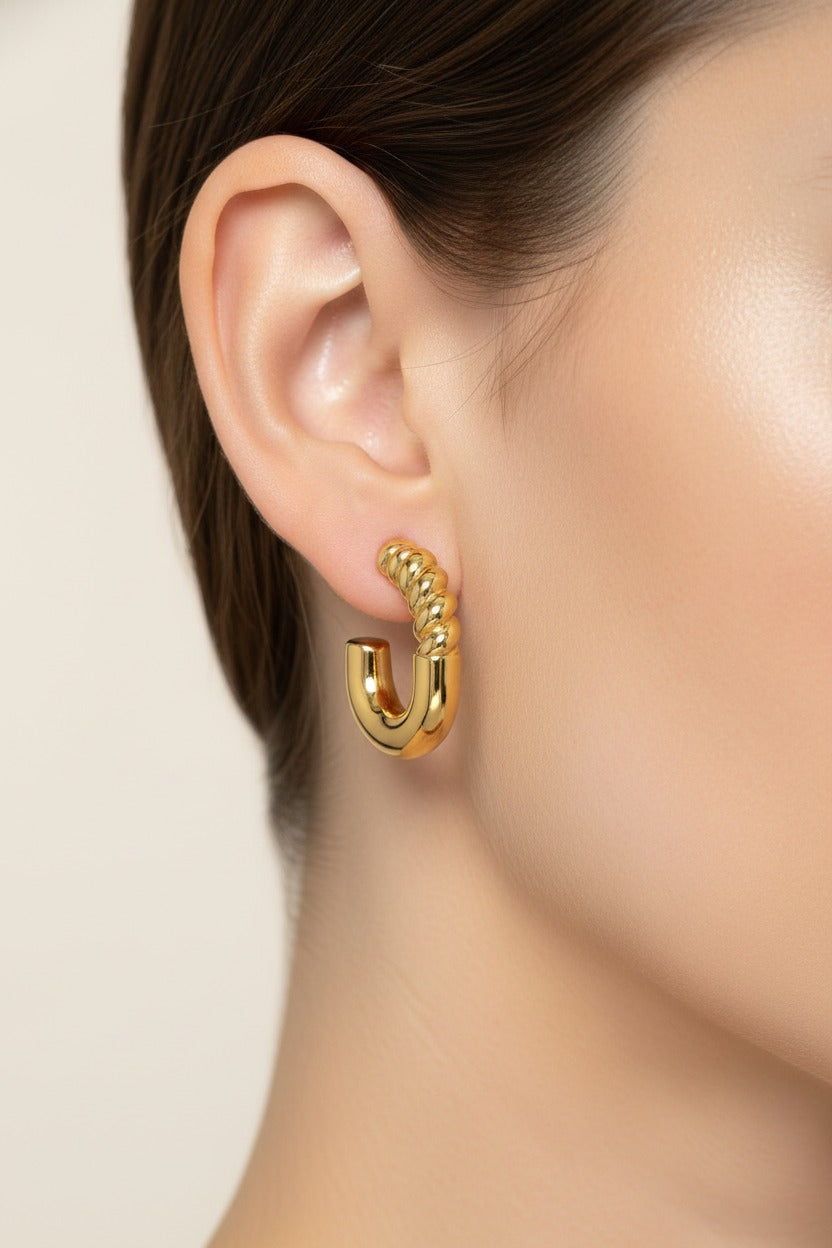Twist curve hoop earrings in 18K PVD gold plated stainless steel worn on ear, showing sculptural twisted detail