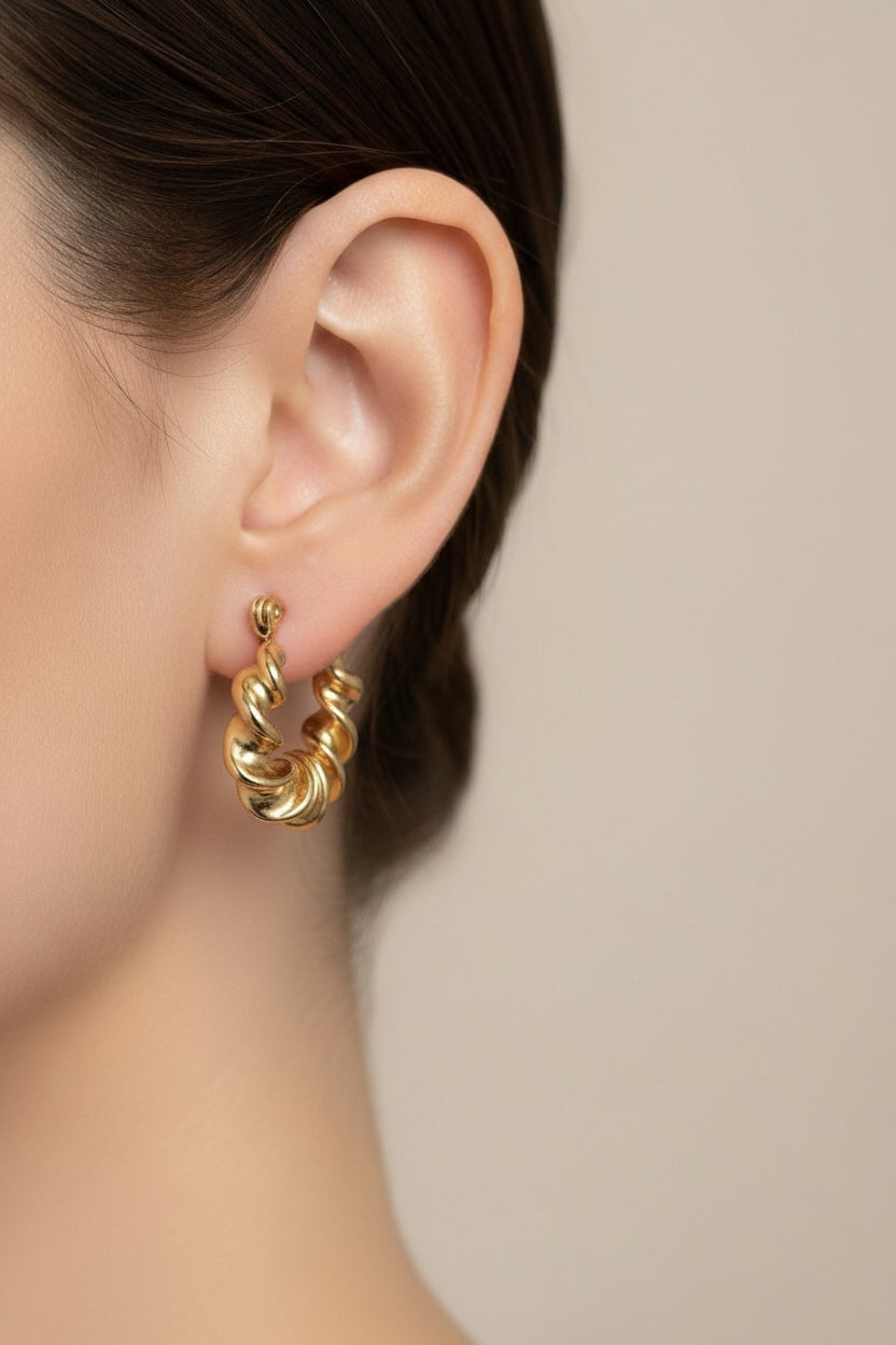 Close-up of twisted hoop earrings in 18K PVD gold plated stainless steel, showcasing a sculptural wavy texture and modern statement design