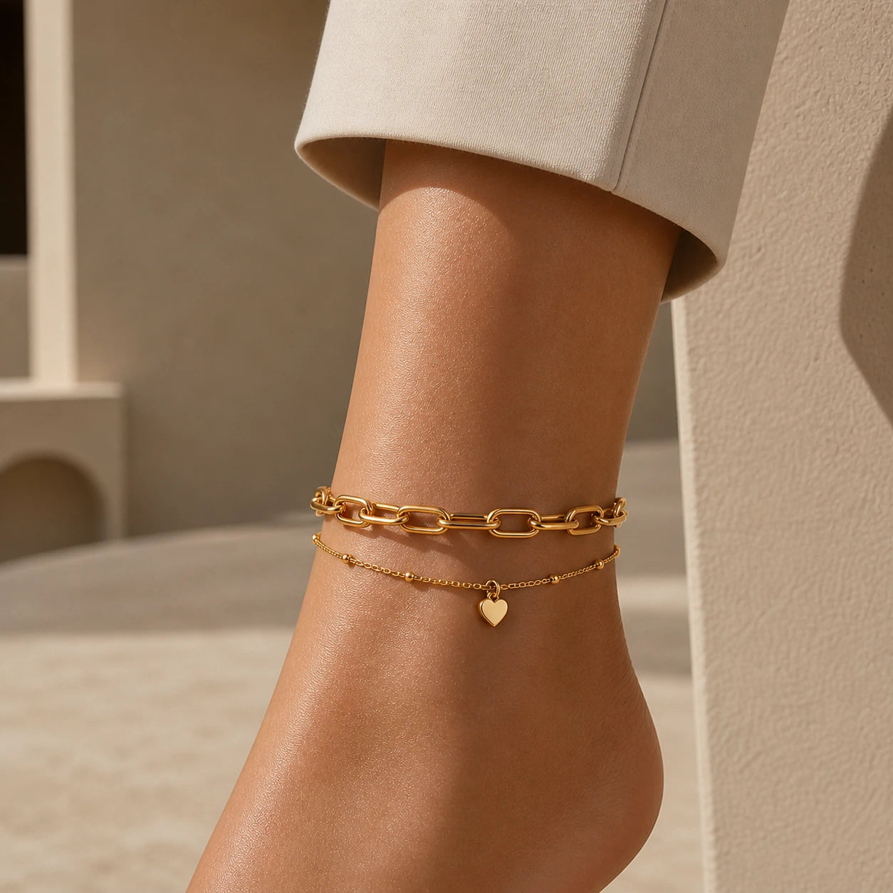 Gold anklets on a person's ankle against a neutral background
