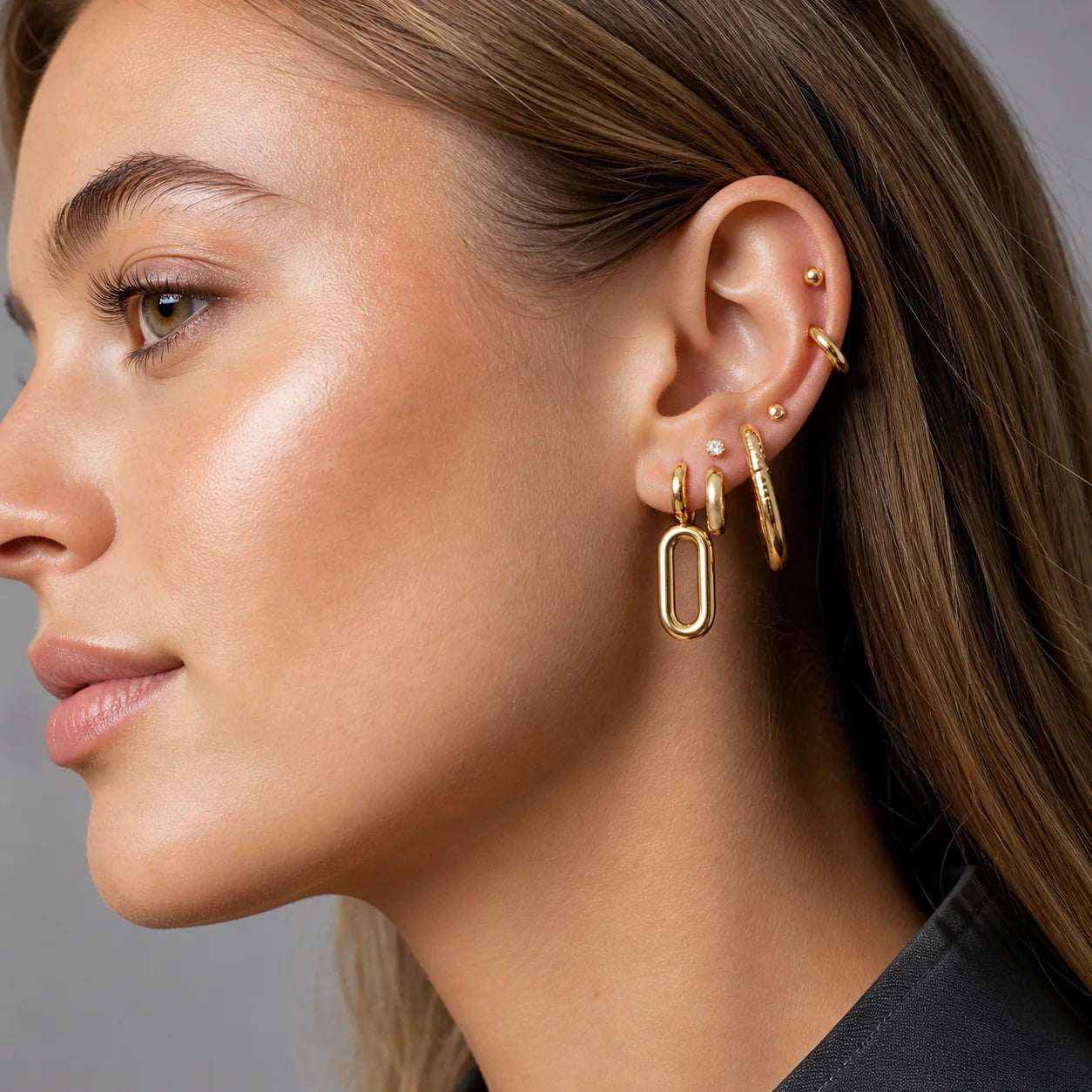 Close-up of a woman's ear with gold earrings against a neutral background