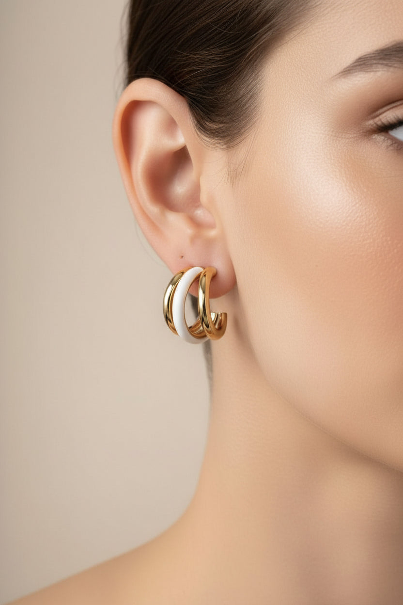 Close-up of double C-hoop earrings in stainless steel with 18K PVD gold plating and white enamel, showcasing a modern layered contrast design