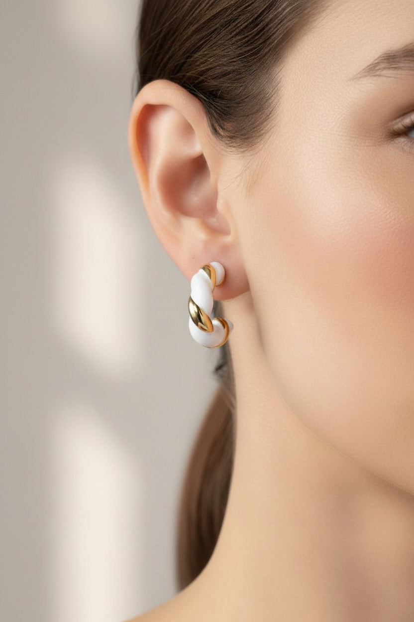 Close-up of twist C-hoop earrings in stainless steel with 18K PVD gold plating, showcasing white and gold twisted detailing and a modern sculptural silhouette
